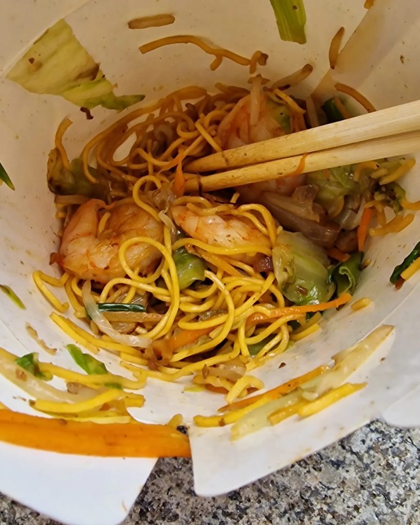 prawn-fried noodles in a takeaway carton, with chopsticks sticking into them